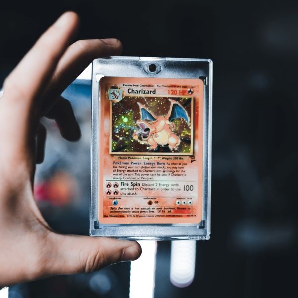 A person holds in their hand a shiny Charizard Pokemon card in a plastic sleeve.