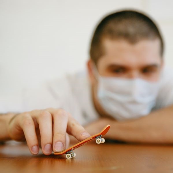 A man holds two fingers on a miniature skateboard popping the world's smallet wheelie.